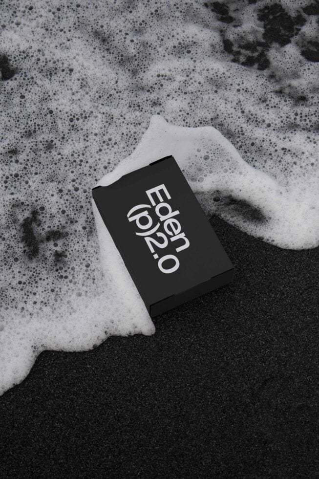 Mockup of a black box labeled Eden p2.0 on wet sand with ocean foam. Perfect for showcasing branding designs with an oceanic or minimalist theme.