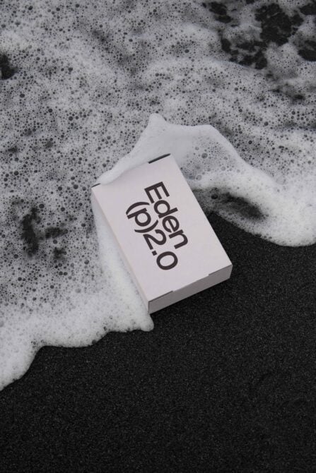 White business card with Eden logo in soapy water, dark wet sand surface