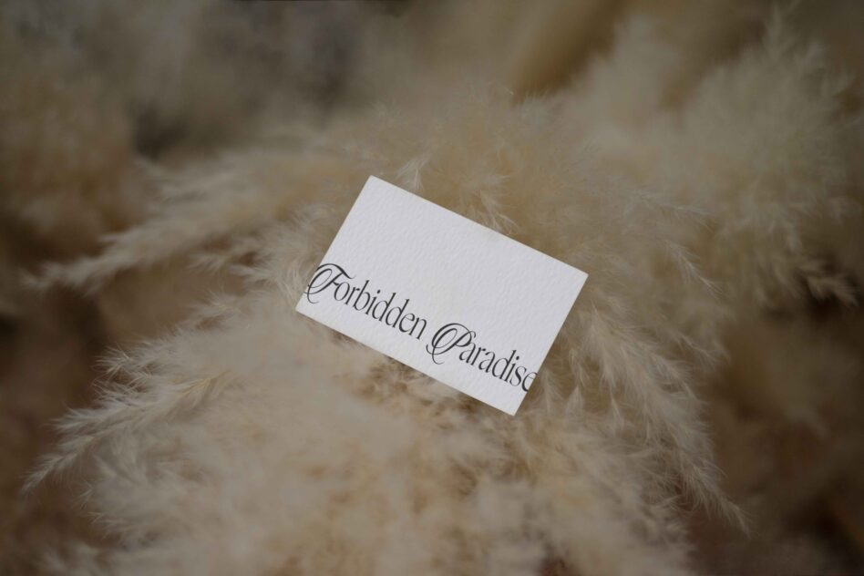 White business card with Forbidden Paradise script resting on soft cream-colored fur texture