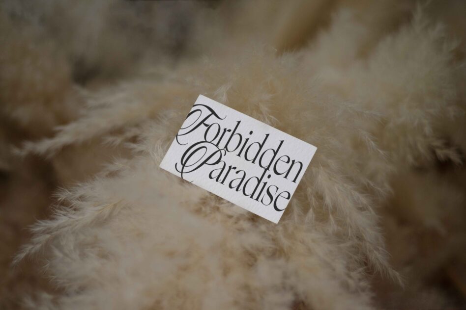 White business card displaying Forbidden Paradise typography on fluffy neutral-toned fabric