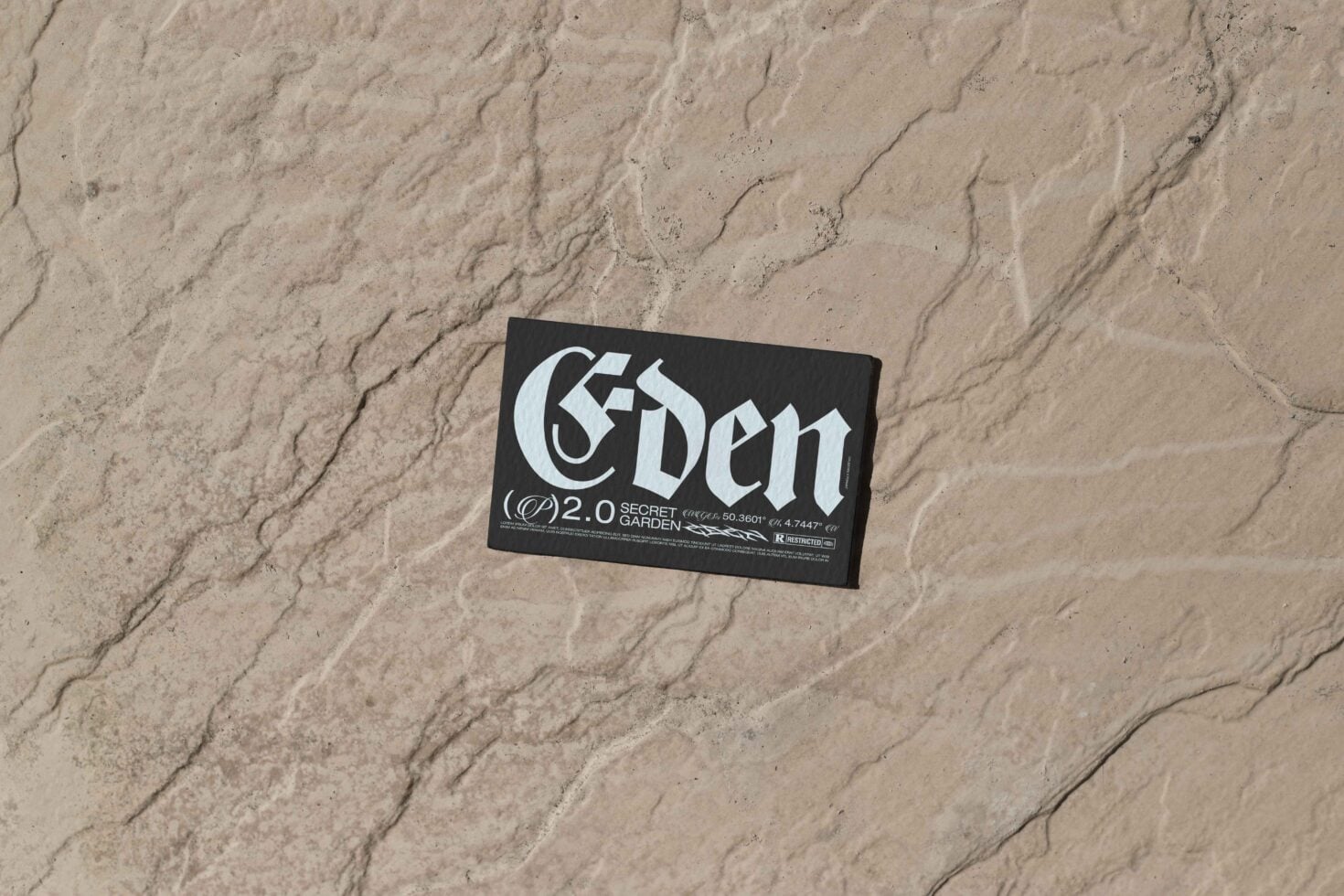 Black business card with 'Eden' lettering sitting on beige sand texture