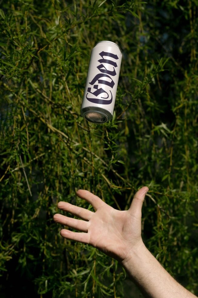 Hand tossing a stylized can design with curvy typography in front of lush greenery. Suitable for graphics mockups templates. Perfect for designers.