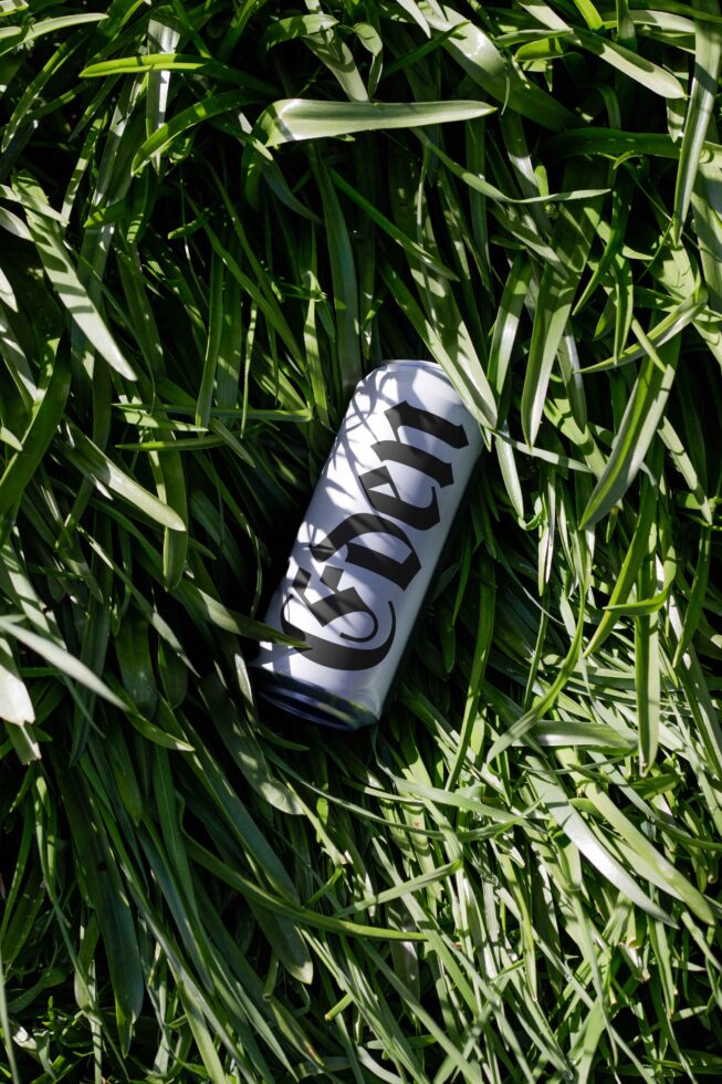 Black can with white striped logo lying in bright green grass