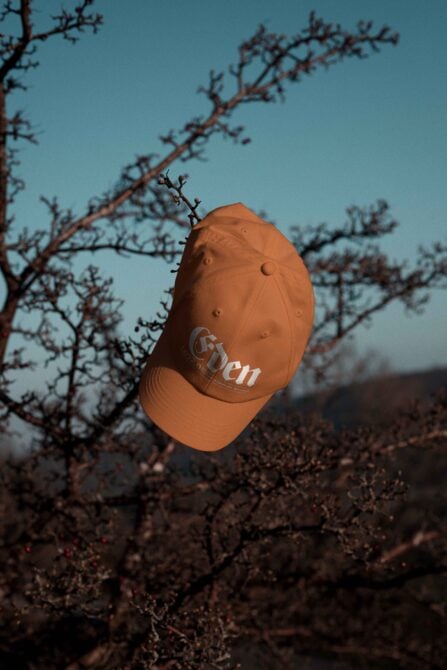 Rust orange cap with Eden embroidered design positioned on dried vegetation landscape
