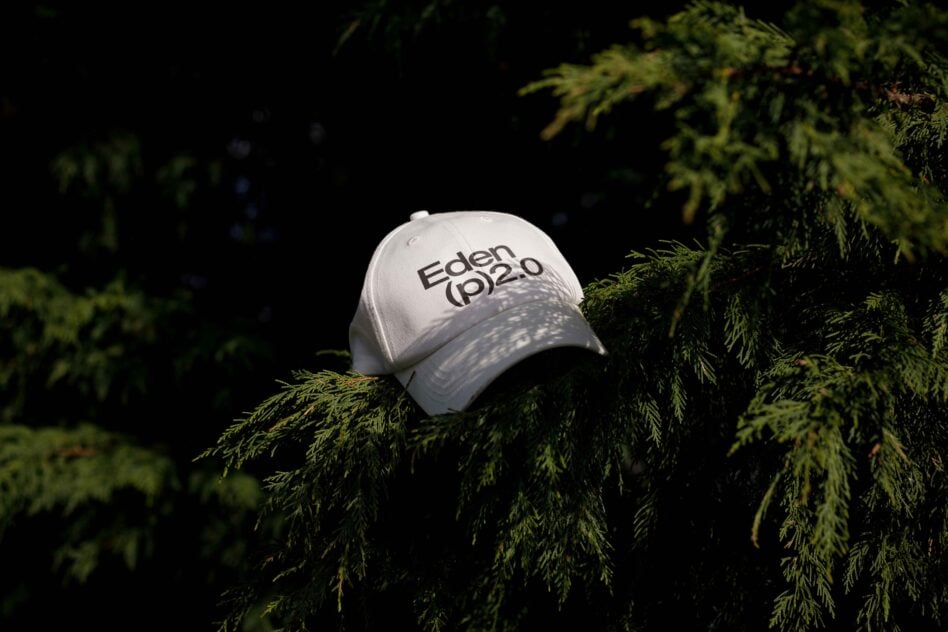 White cap with words Eden 2.0 displayed on pine branches with dark green foliage. Stylish cap mockup for designers. Nature themed fashion accessory.