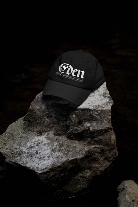 Black cap with Eden branding positioned on textured stone surface in low light