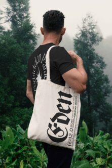 Back shot of person carrying cream tote with large serif lettering in woods