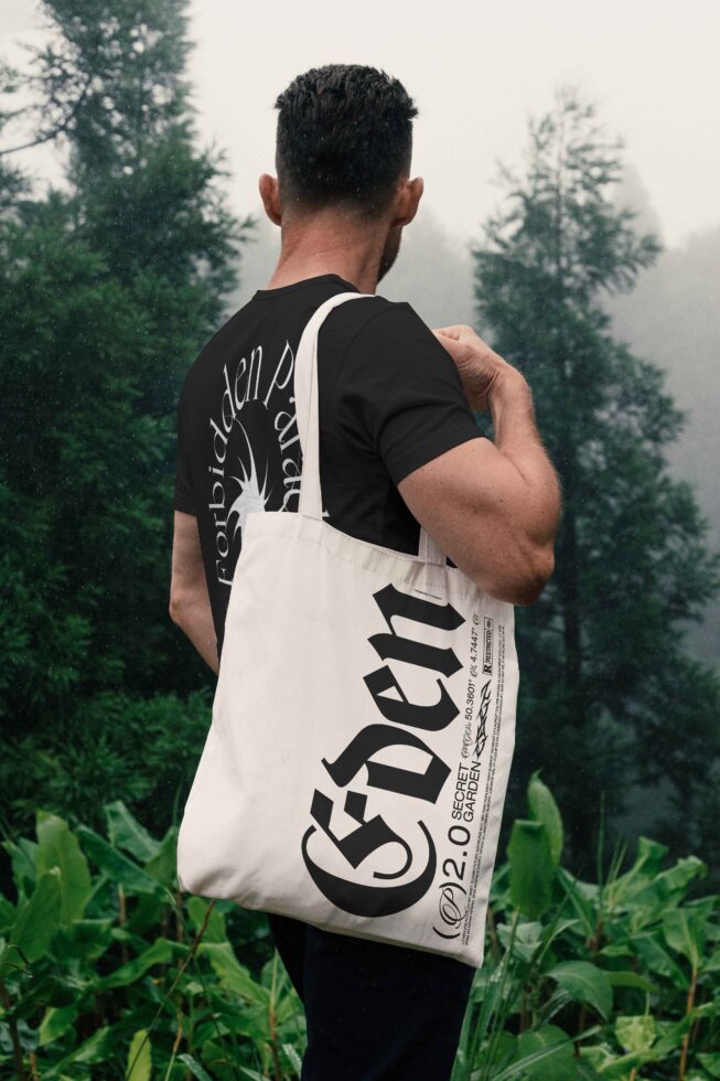 Back shot of person carrying cream tote with large serif lettering in woods