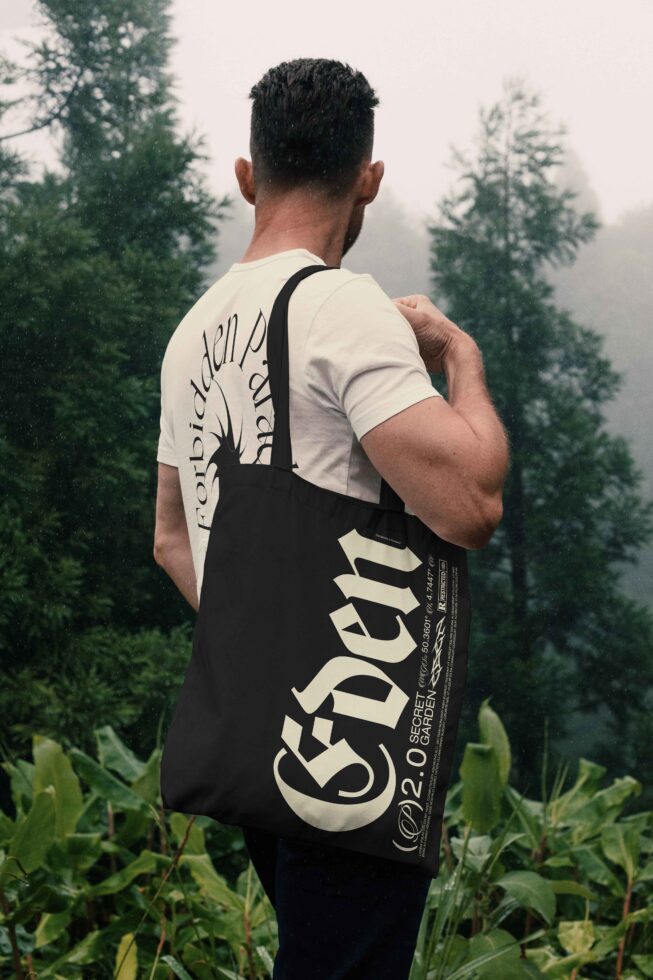 Model wearing black tote bag with bold typography over shoulder in nature