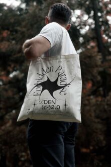 Person wearing white tote bag with bold serif branding in forest setting