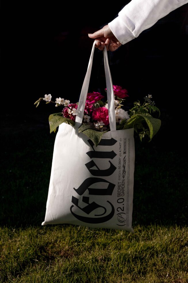 Hand holding cream tote filled with magenta peonies, baby's breath, over grass