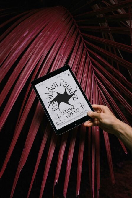 iPad held up showing typography design with dark star shape on cream background, magenta palm fronds overhead