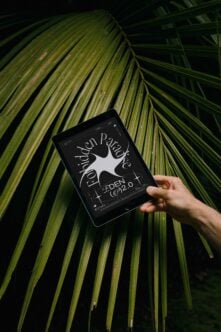 Tablet displaying Forbidden Paradise design held over palm leaf background. Ideal for showcasing graphic design mockups for creative designers and artists.