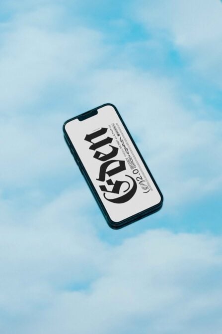 Dark teal iPhone displaying bold serif typography on white screen against soft blue sky background
