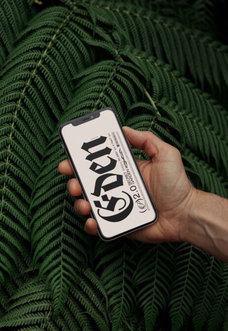 Hand holding smartphone displaying bold font design mockup titled Eden near green ferns. Ideal for designers seeking typography inspiration and templates.