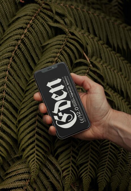 Hand holding phone with bold gothic font design Eden displayed against a background of lush green ferns ideal for showcasing typography templates.