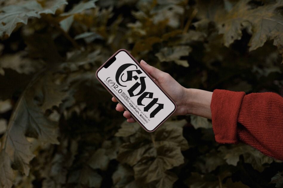 Hand holding pink-rimmed phone displaying bold black typography on white screen against leafy background