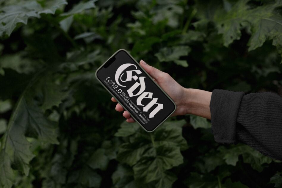 Hand holding phone with bold geometric logo design on black screen against leafy green background
