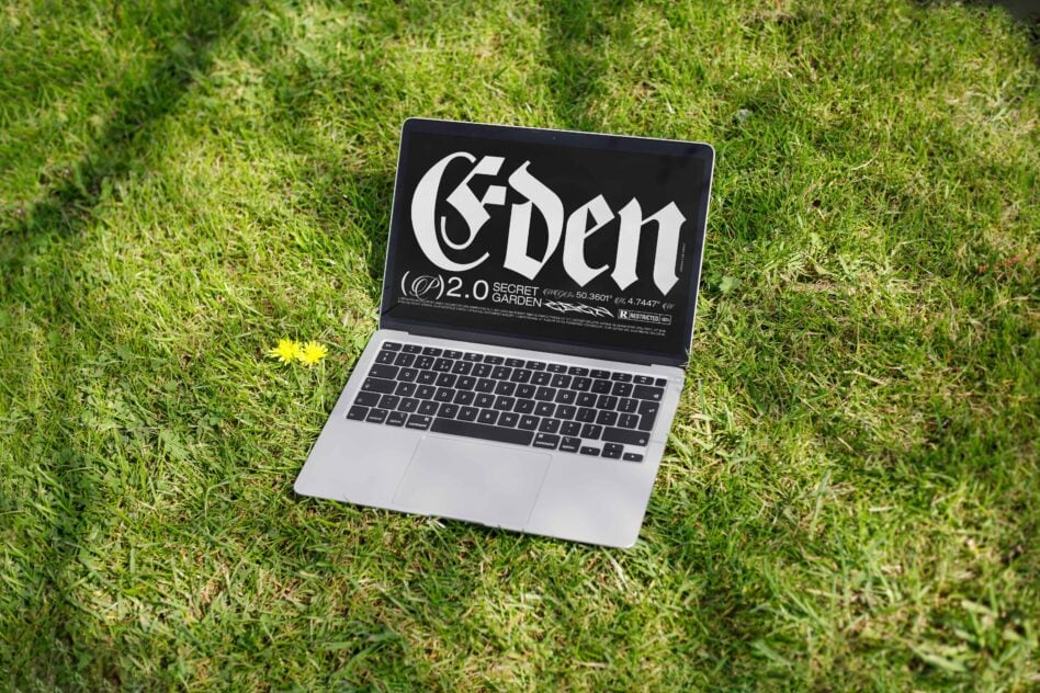 Silver laptop showing dark Eden design on green grass with yellow flower