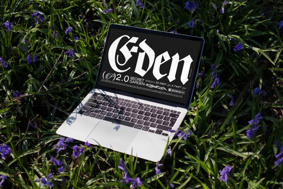 Laptop displaying gothic font design lies on grass amid purple flowers. Perfect for digital mockups and typography projects in natural settings.