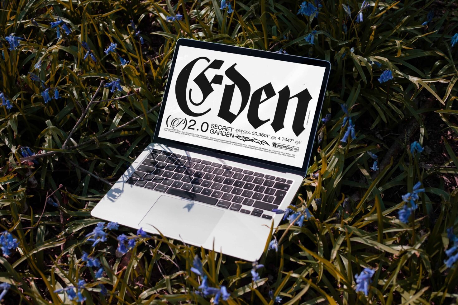 Laptop displaying bold Gothic typography design in a natural setting with blue flowers for designers. Ideal for fonts category in digital asset marketplace.