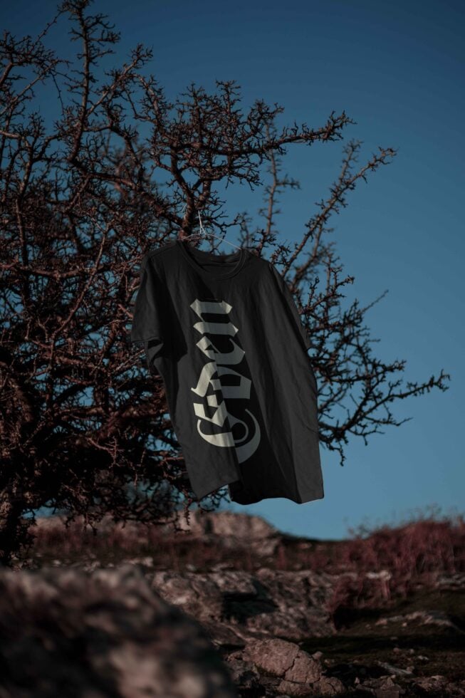 Outdoor t-shirt mockup with bold Gothic font; black shirt against a natural backdrop; creative apparel design concept; digital asset for designers.