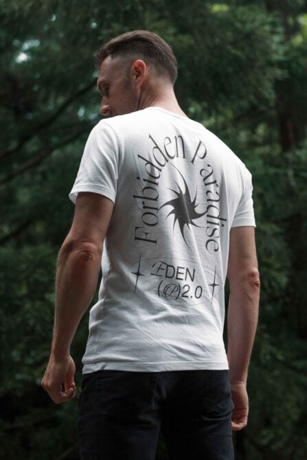 Man wearing white t-shirt with bold graphic design Forbidden Paradise print outdoors fashion mockup apparel template stylish typography trunks trees.