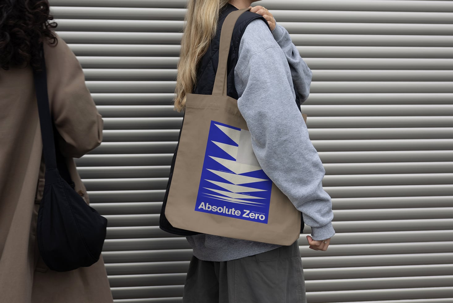 Woman carrying beige tote bag with blue zigzag logo print on it