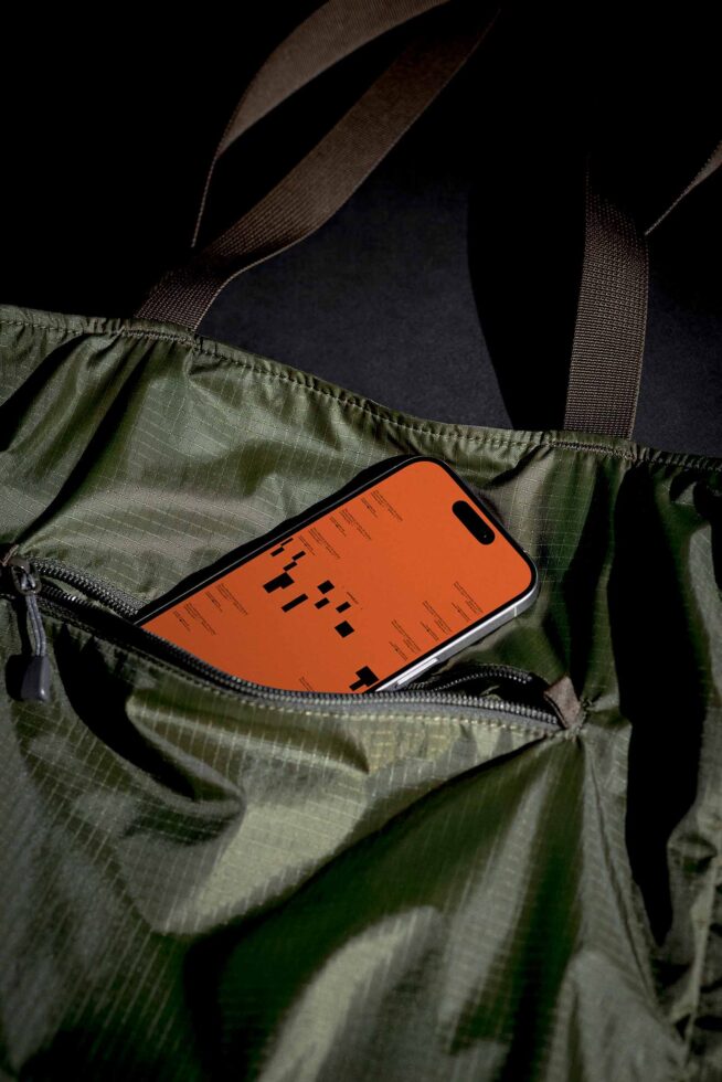 Smartphone mockup in green tote bag with orange screen design. Ideal for showcasing app UI UX graphics in lifestyle settings. Perfect for designers.
