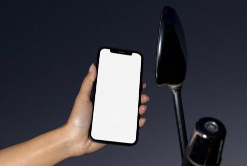 Hand holding smartphone mockup with a blank white screen next to a motorcycle mirror on a dark background ideal for app design presentations