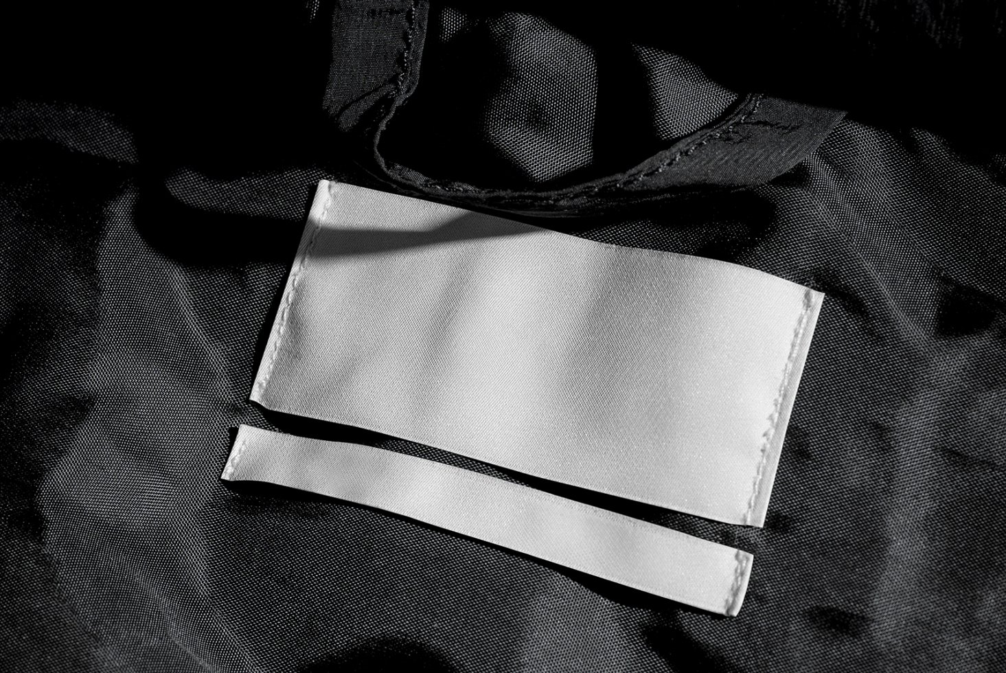 Black fabric texture with two blank white clothing labels suitable for apparel mockups. High-resolution textile design asset for fashion designers.