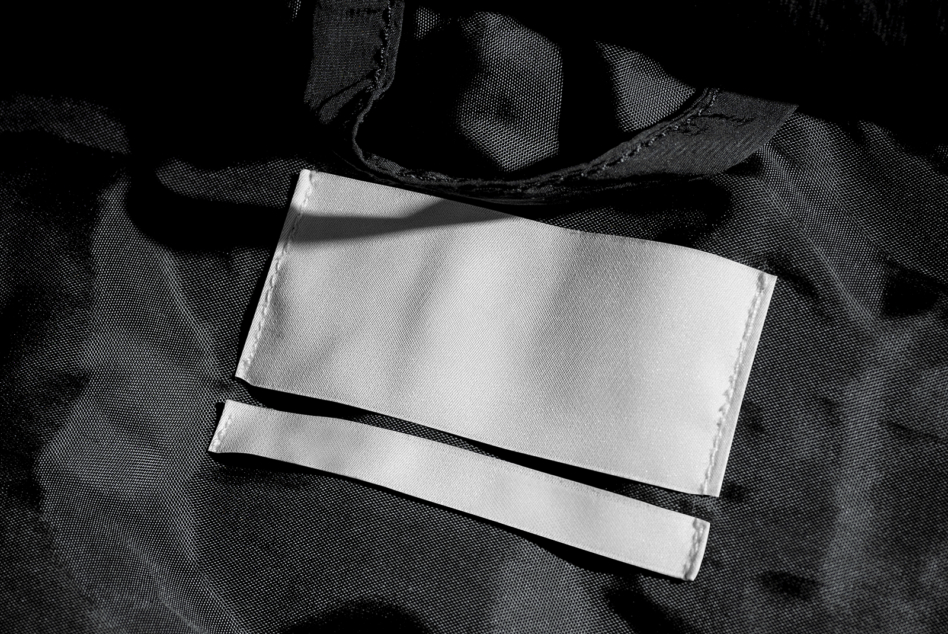Blank white garment label mockup on black plaid fabric background