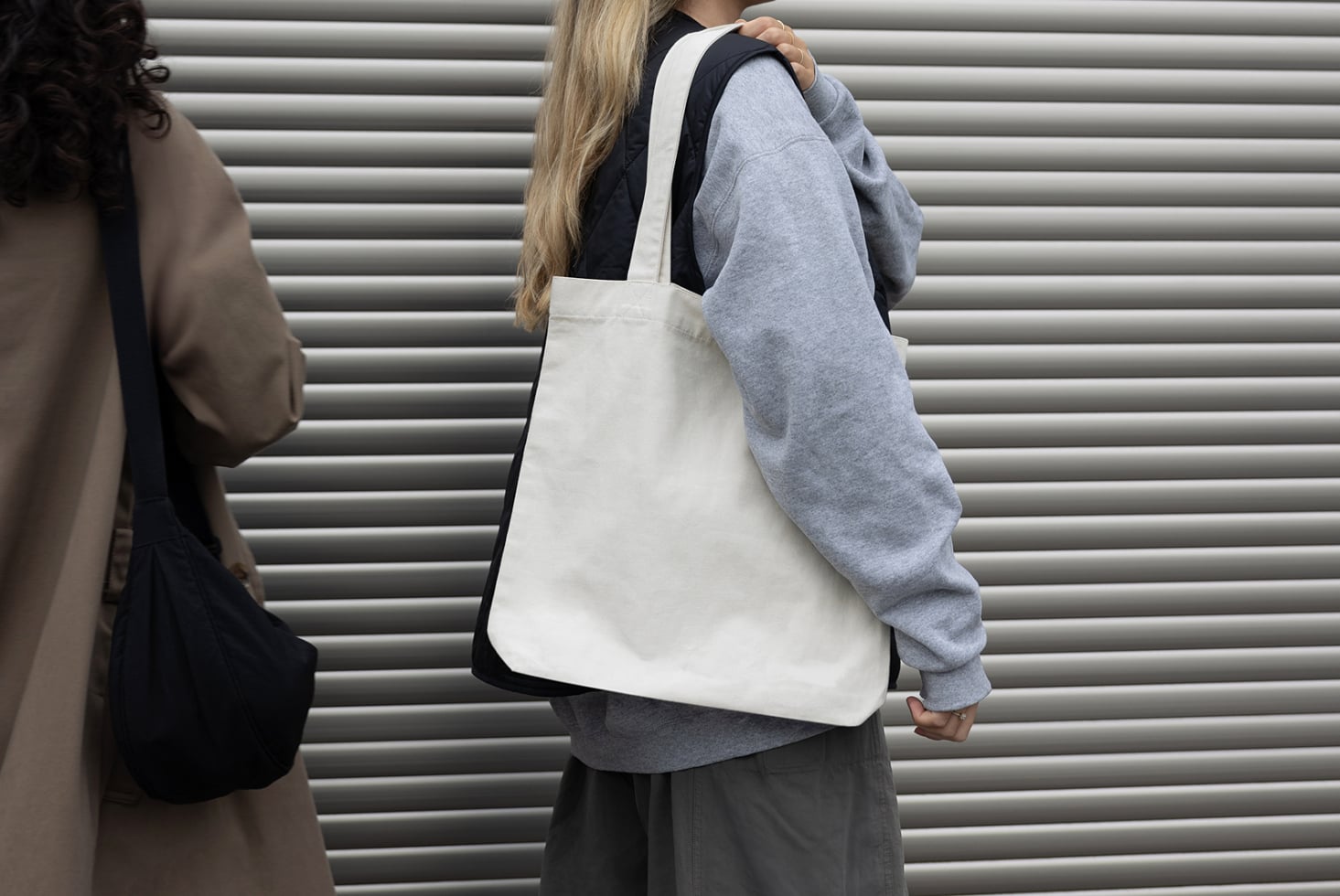 Woman wearing blank cream canvas tote bag against metal shutter wall