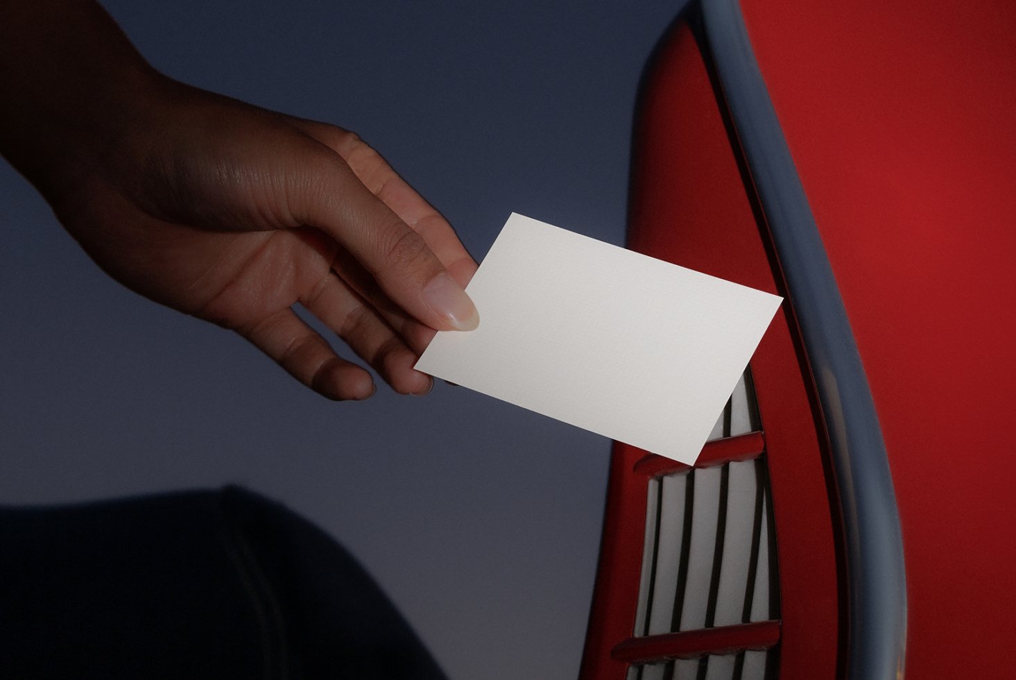 Hand holding blank business card against red metallic surface suitable for mockups; ideal for showcasing branding, logo design, and business card templates.