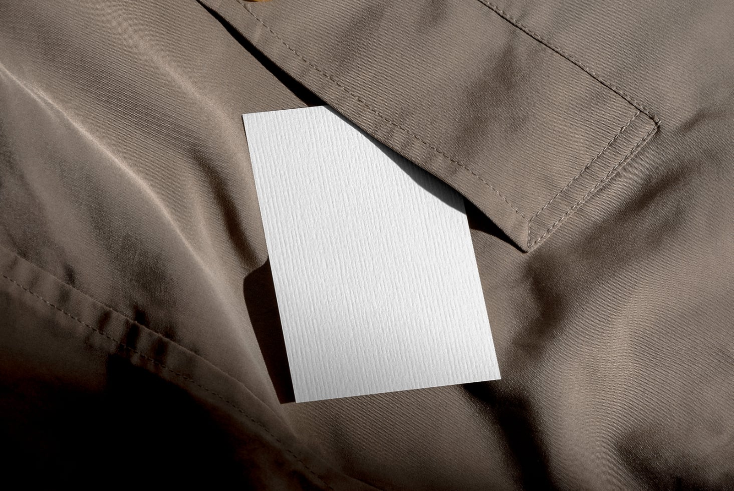 Blank white card on textured beige fabric with dramatic shadow cast by window light