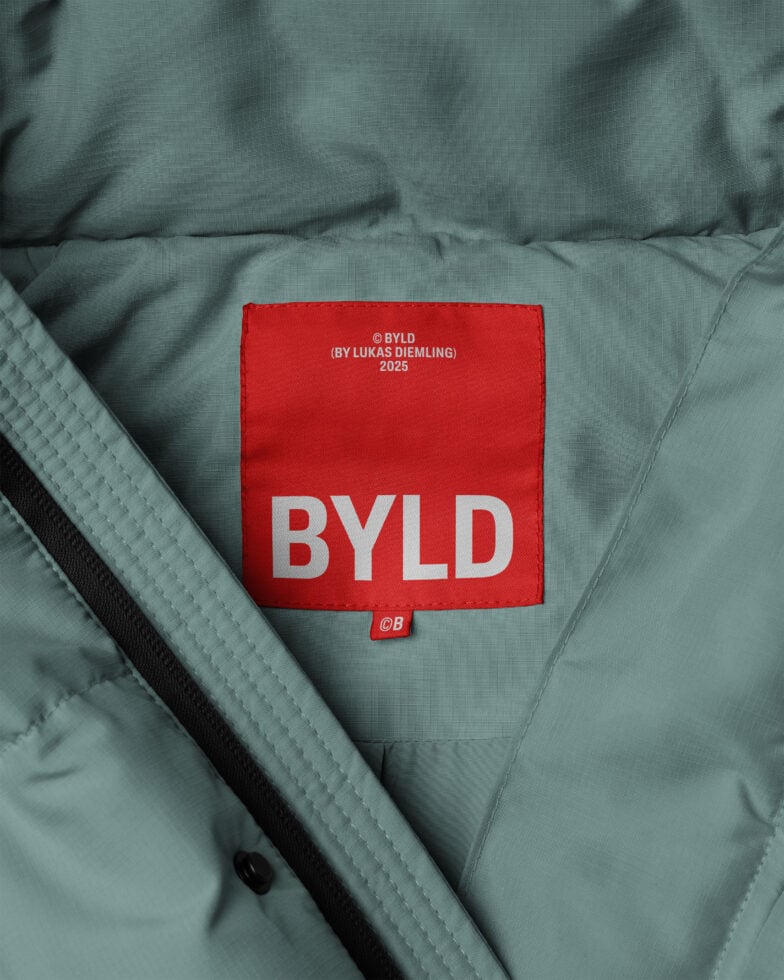 Green jacket close-up featuring a bold red label with the text BYLD in white. Ideal for apparel mockup designs fashion template branding graphics.