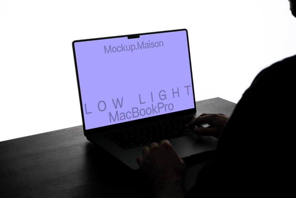 Hands holding MacBook Pro showing purple screen in low light setup