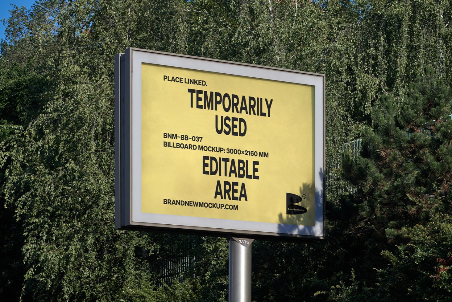 Yellow billboard mockup on pole against tall green trees, clear sky