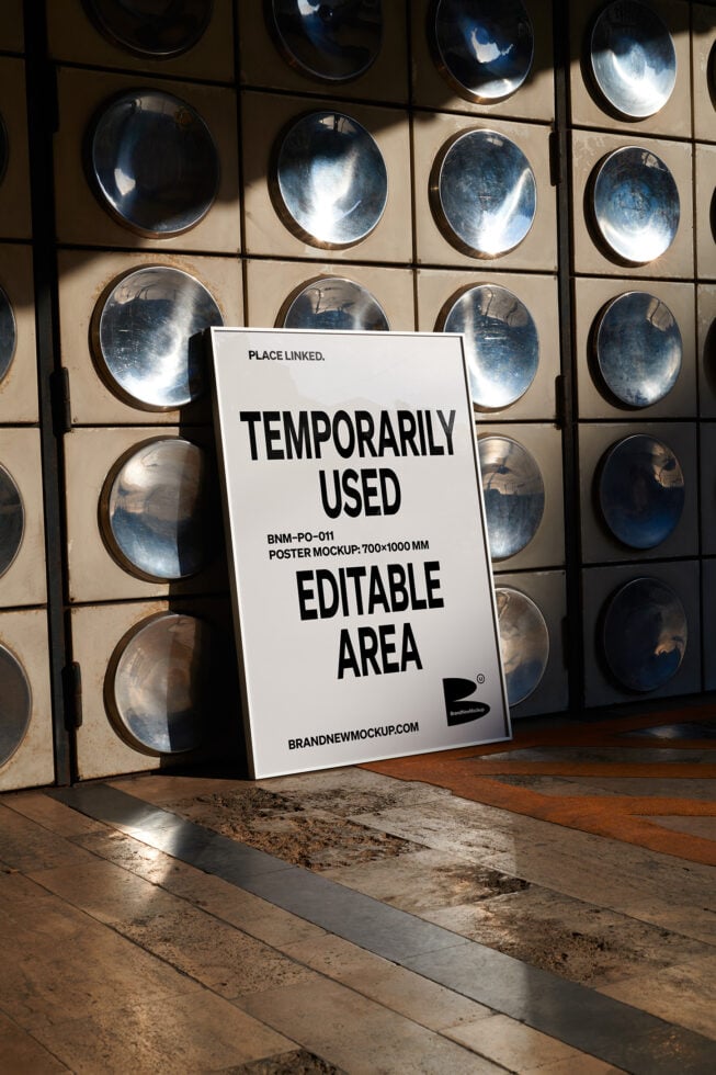 Leaning white poster mockup against metallic circular wall installation in sunlight