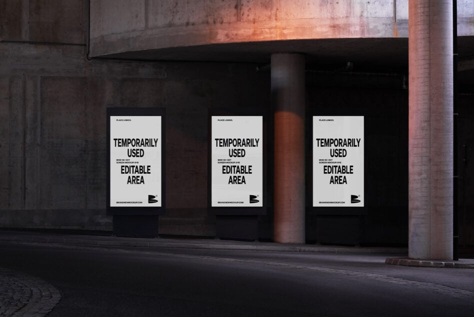 Three white posters on dark storefront at night with industrial column between them