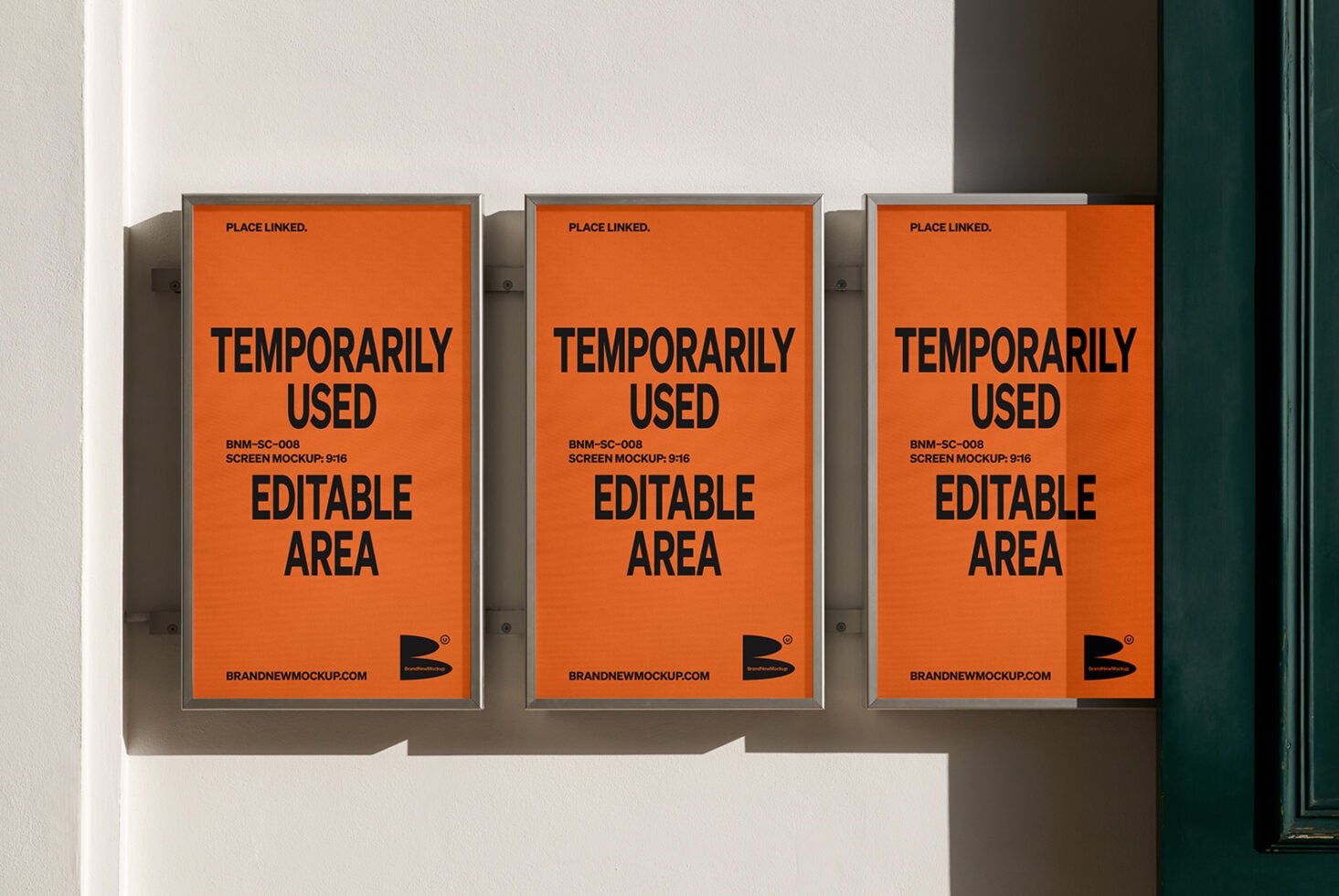 Three orange framed posters on white wall with strong side shadows, green door visible right