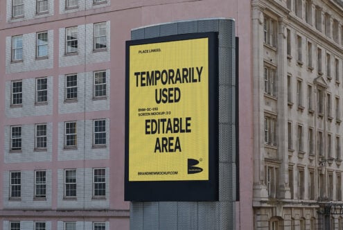 Building facade with a large billboard showcasing a yellow screen mockup template for designers. Editable area for custom designs. Urban backdrop.