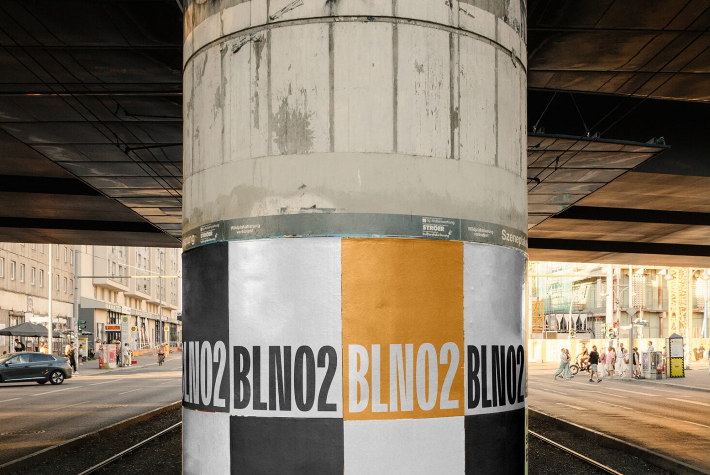 Concrete column wrapped with yellow, black, white repeating brand name pattern on urban plaza