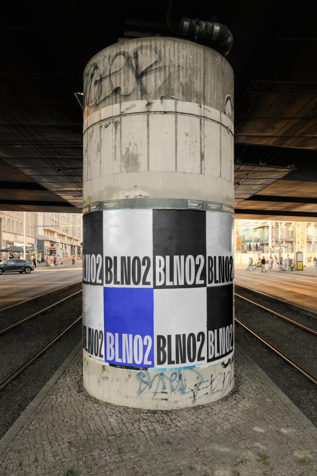 Weathered concrete column wrapped with black, white, blue repeating brand name pattern