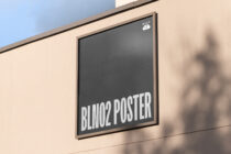 Framed charcoal-gray poster on cream wall with white text reading BLINO2 POSTER