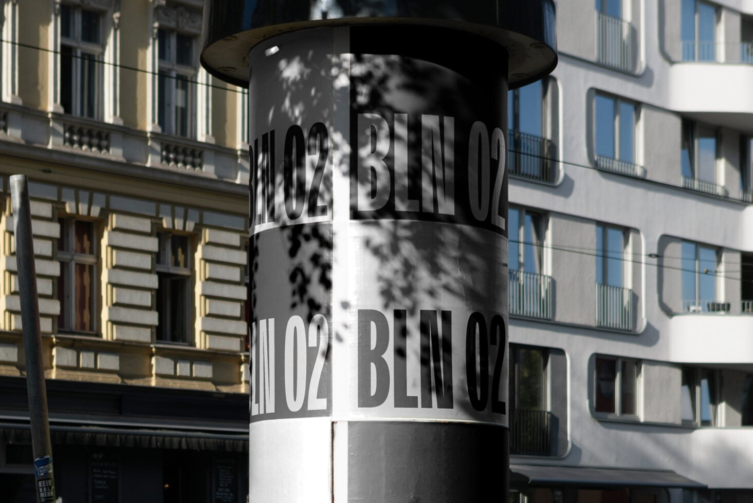 Cylindrical bollard wrapped with repeating Berlin postal code text casting shadows