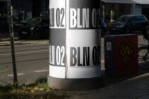 Street bollard wrapped in black white bands with bold Berlin typography during daytime