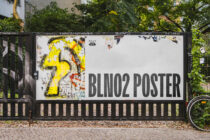 White billboard with yellow graffiti art on left, dark gray text reads BLINO2 POSTER