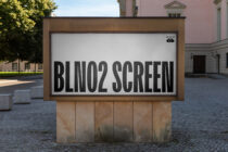 Street billboard with bold black text on white background mounted on stone base