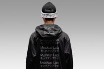 Back view of black windbreaker with white beanie on grey background